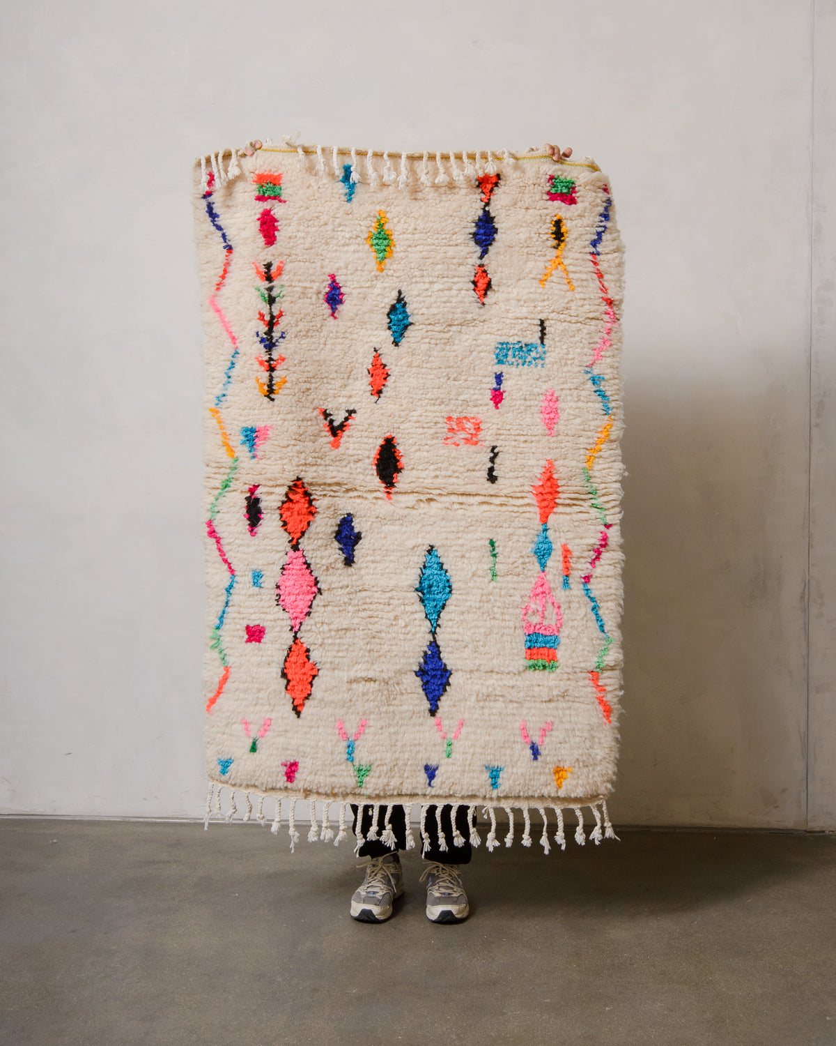 Berberlin Azilal rug in cream wool with colourful cotton being held up in front of a white wall.